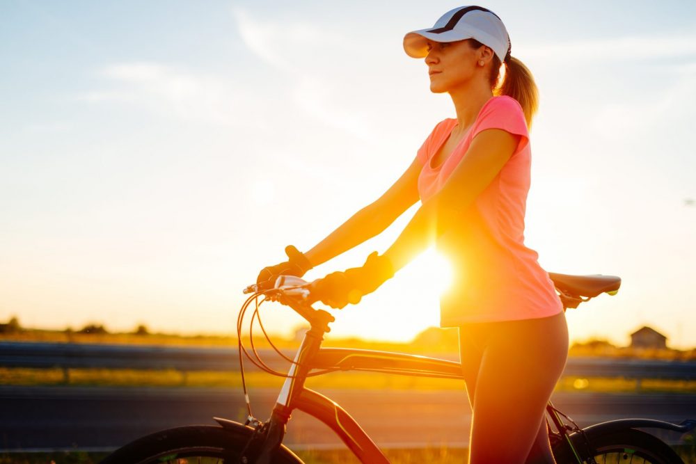 Portrait of beautiful muscular woman holding grips of bike steering bar on sunny summer day in sunset, after exhausting ride. Woman is wearing cap and dressed in sports clothing. Location: Novi Sad, Serbia, Europe